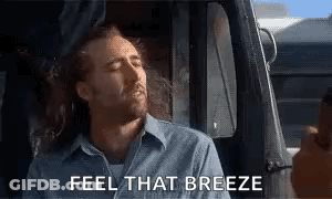 A Man Is Sitting In The Driver 'S Seat Of A Truck With His Eyes Closed And The Words `` Feel That Breeze '' . GIF