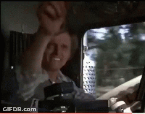 A Man Is Sitting In The Driver 'S Seat Of A Truck With His Hand In The Air GIF