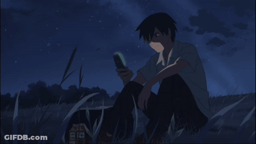 A Man Is Sitting In The Grass Looking At His Cell Phone GIF