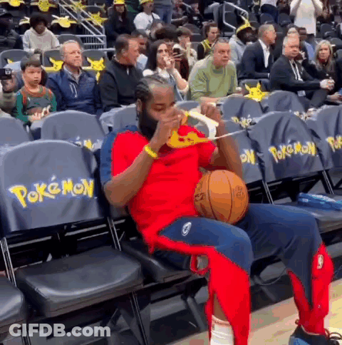 A Man Is Sitting In The Stands Holding A Basketball And Eating Pizza . GIF