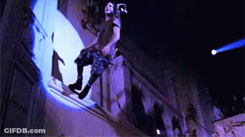 A Man Is Sitting On A Balcony With A Camera On His Head . GIF