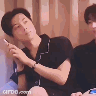 A Man Is Sitting On A Bed Smoking A Cigarette While Another Man Looks On . GIF