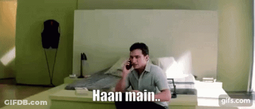 A Man Is Sitting On A Bed Talking On A Cell Phone With The Words Haan Main . GIF