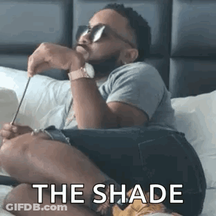 A Man Is Sitting On A Bed Wearing Sunglasses And Holding A Pair Of Scissors . GIF
