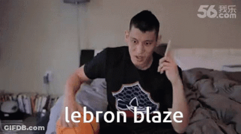 A Man Is Sitting On A Bed With A Basketball And The Word Lebron Blaze On His Shirt GIF
