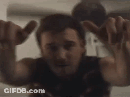 A Man Is Sitting On A Bed With His Arms Outstretched And Making A Hand Sign . GIF