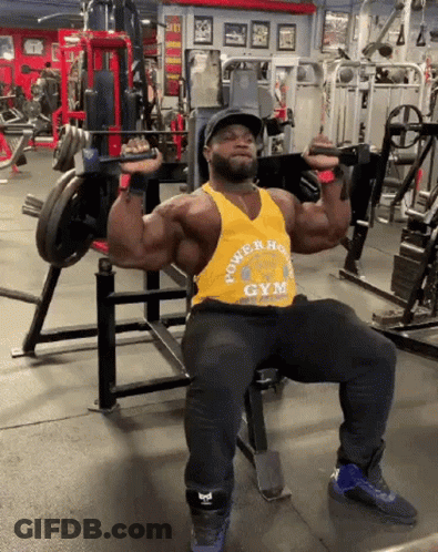 A Man Is Sitting On A Bench In A Gym With A Barbell In His Hands . GIF