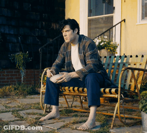 A Man Is Sitting On A Bench With A Bowl Of Food In His Hand GIF