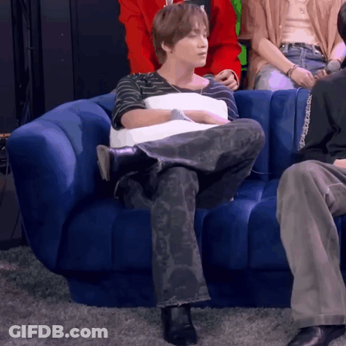 A Man Is Sitting On A Blue Couch Holding A Pillow . GIF