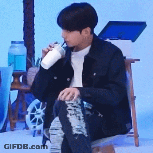 A Man Is Sitting On A Chair Drinking From A Cup . GIF
