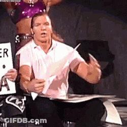 A Man Is Sitting On A Chair Holding A Piece Of Paper And A Woman Is Standing Behind Him . GIF