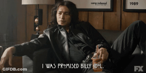 A Man Is Sitting On A Couch And Says " I Was Promised Billy Idol " While Holding A Cup GIF