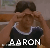 A Man Is Sitting On A Couch Covering His Eyes With His Hands And The Word Aaron Is On The Bottom . GIF