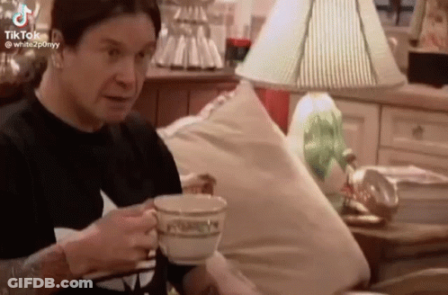 A Man Is Sitting On A Couch Drinking A Cup Of Tea . GIF