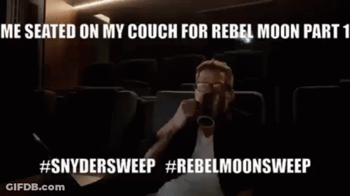 A Man Is Sitting On A Couch Drinking From A Cup In A Theater . GIF