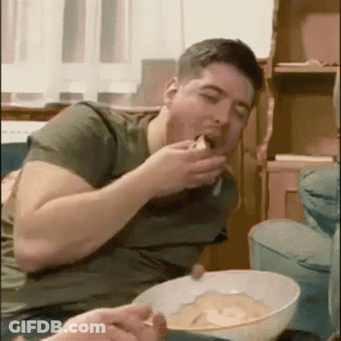 A Man Is Sitting On A Couch Eating A Bowl Of Food GIF