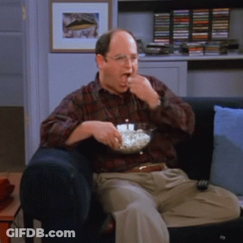 A Man Is Sitting On A Couch Eating Popcorn GIF