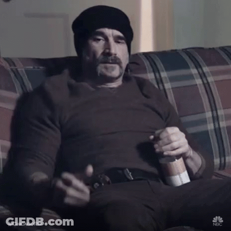 A Man Is Sitting On A Couch Giving A Thumbs Up Sign While Holding A Bottle Of Beer . GIF