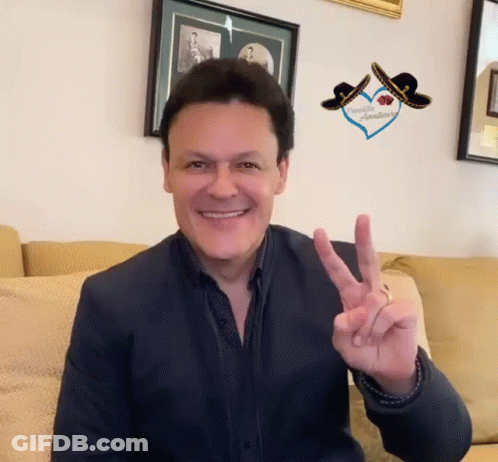 A Man Is Sitting On A Couch Giving The Peace Sign GIF