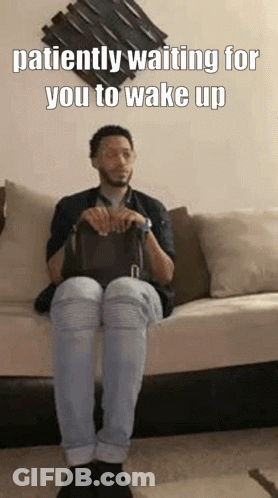 A Man Is Sitting On A Couch Holding A Bag And Waiting For Someone To Wake Up . GIF