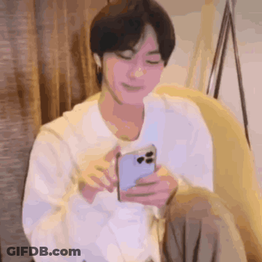 A Man Is Sitting On A Couch Holding A Cell Phone In His Hand . GIF