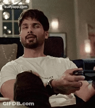 A Man Is Sitting On A Couch Holding A Cell Phone In His Hand . GIF