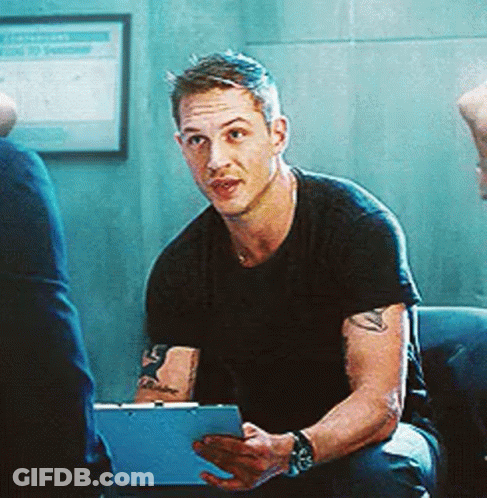 A Man Is Sitting On A Couch Holding A Clipboard And Looking At The Camera . GIF