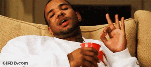A Man Is Sitting On A Couch Holding A Cup Of Coffee And Making An Ok Sign . GIF
