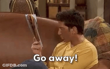 A Man Is Sitting On A Couch Holding A Magazine And Saying `` Go Away '' . GIF