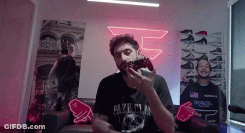 A Man Is Sitting On A Couch Holding A Video Game Controller In His Hand . GIF