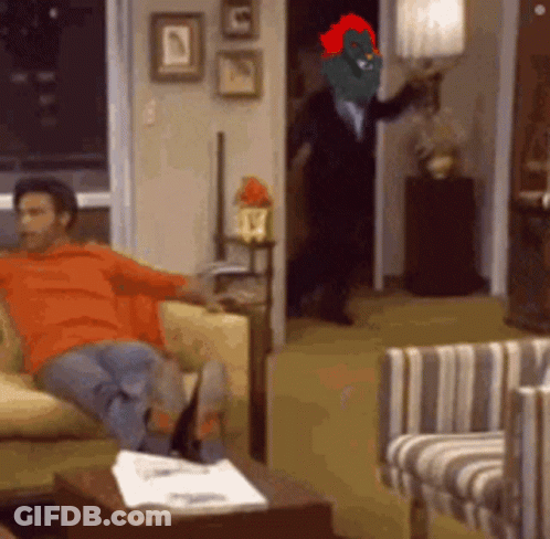 A Man Is Sitting On A Couch In A Living Room With A Cartoon Character On His Head GIF