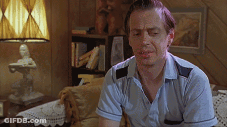 A Man Is Sitting On A Couch In A Living Room With A Lamp In The Background . GIF