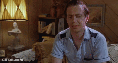 A Man Is Sitting On A Couch In A Living Room With A Lamp . GIF