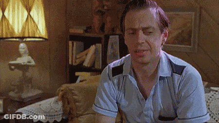A Man Is Sitting On A Couch In A Living Room With His Eyes Closed And A Lamp In The Background . GIF