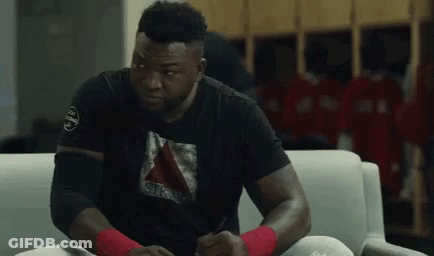 A Man Is Sitting On A Couch In A Locker Room Wearing A Black Shirt . GIF