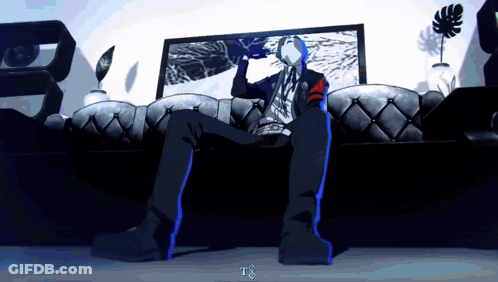 A Man Is Sitting On A Couch In Front Of A Tv With The Letter T On The Bottom Right GIF