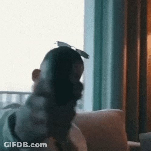 A Man Is Sitting On A Couch In Front Of A Window Wearing Sunglasses And A Mask . GIF