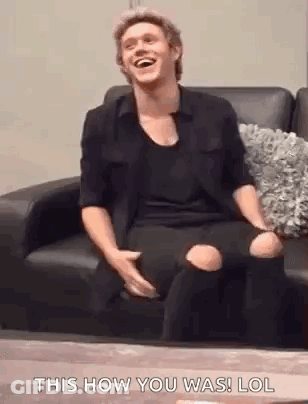 A Man Is Sitting On A Couch Laughing And Holding His Knee . GIF