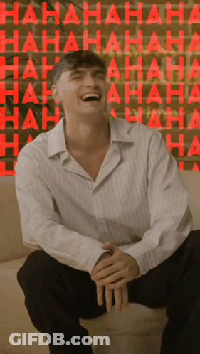 A Man Is Sitting On A Couch Laughing In Front Of A Wall That Says ' Hahaha ' GIF