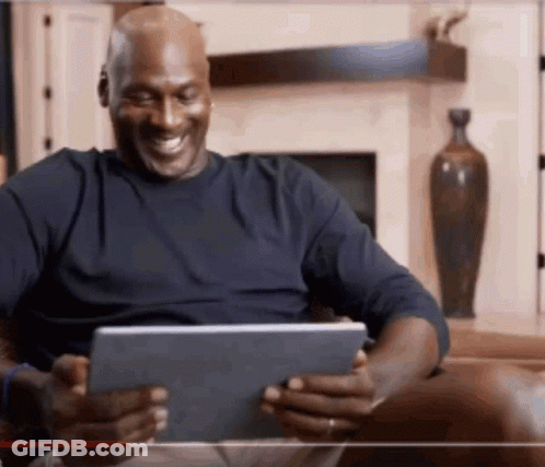 A Man Is Sitting On A Couch Looking At A Tablet And Smiling . GIF