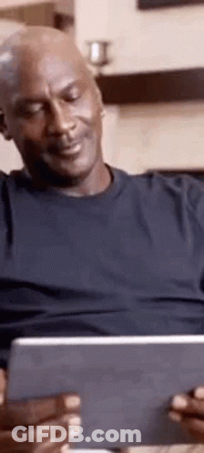 A Man Is Sitting On A Couch Looking At A Tablet Computer . GIF
