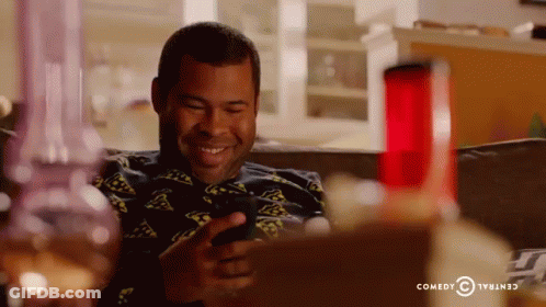 A Man Is Sitting On A Couch Looking At His Phone With A Comedy Central Logo In The Background GIF