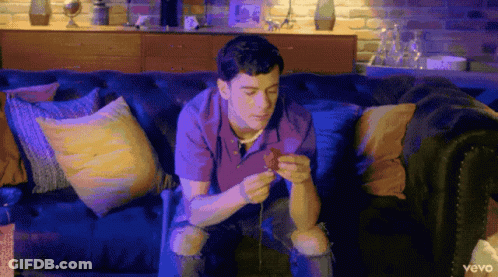 A Man Is Sitting On A Couch Looking At His Phone With The Word Vevo On The Bottom Left GIF