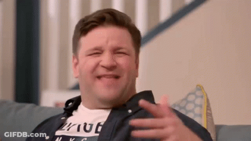 A Man Is Sitting On A Couch Making A Funny Face While Laughing . GIF