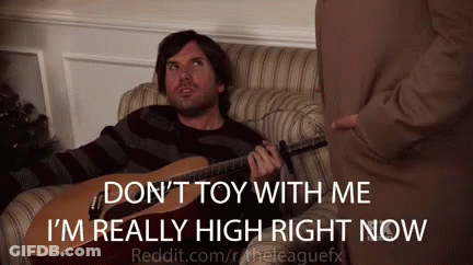 A Man Is Sitting On A Couch Playing A Guitar And Talking To Another Man GIF