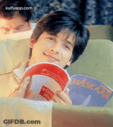 A Man Is Sitting On A Couch Reading A Book And Smiling . GIF