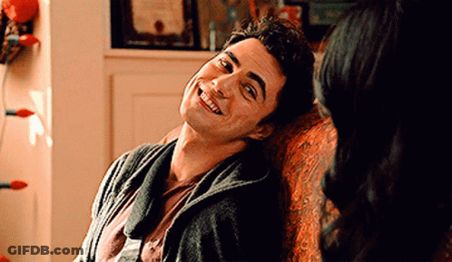 A Man Is Sitting On A Couch Smiling At A Woman GIF