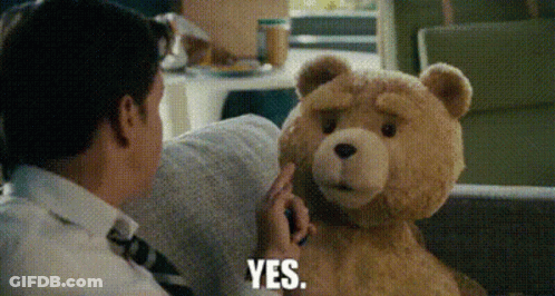 A Man Is Sitting On A Couch Talking To A Teddy Bear Who Is Saying Yes GIF