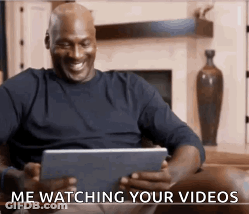 A Man Is Sitting On A Couch Watching A Video On A Tablet And Smiling . GIF