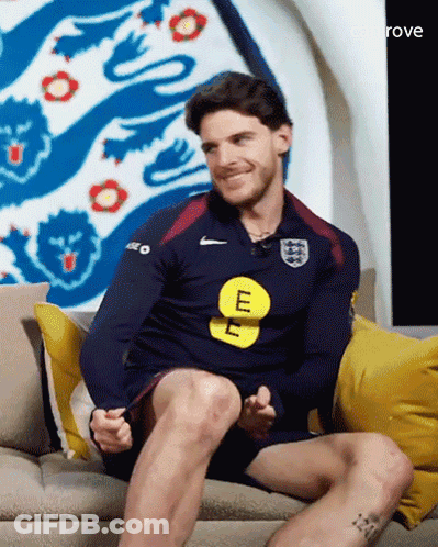 A Man Is Sitting On A Couch Wearing A Blue Nike Shirt With The Letter E On It GIF